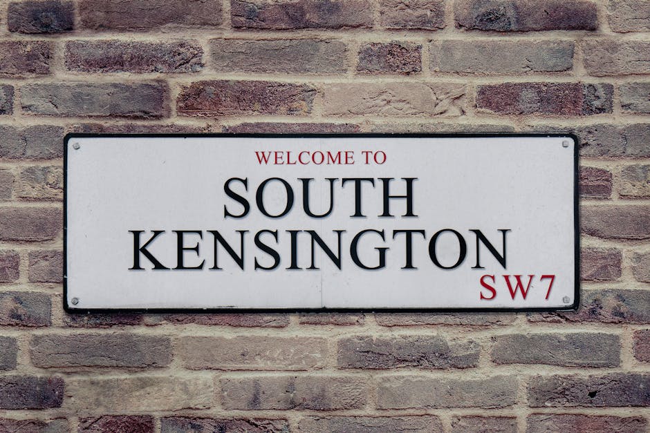 The image shows a quiet residential street in Kennington with tall, ornate terraced houses featuring light-colored facades, decorative window surrounds, and small balconies. Several large cardboard bo
